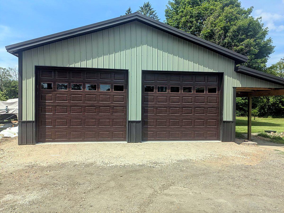 Sage green pole barn garage with two brown overhead doors and covered lean-to