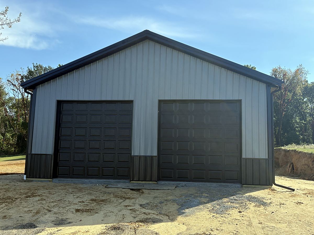 Gray pole barn garage with black wainscot and two black overhead doors