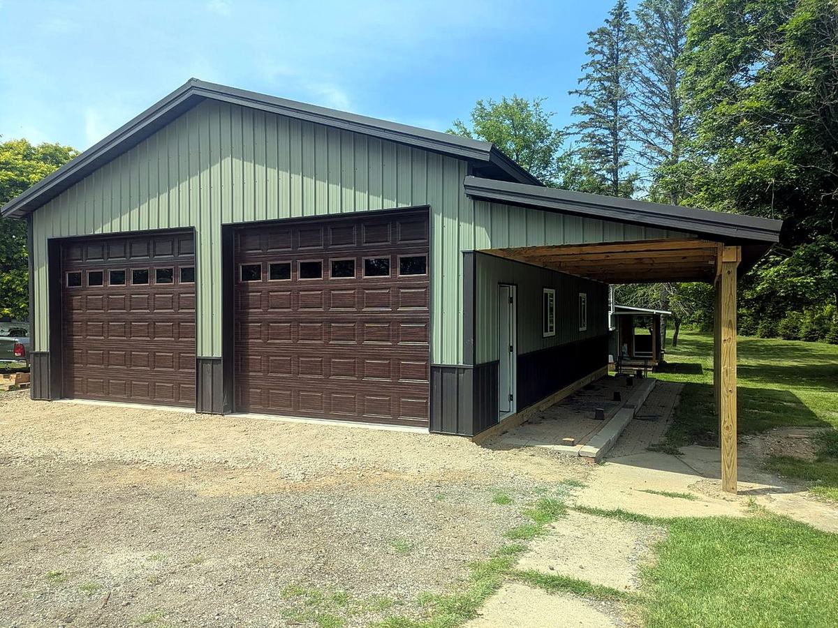 Sage green pole barn garage with brown overhead doors and covered lean-to