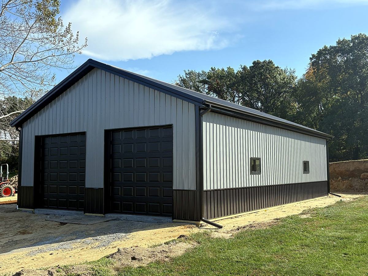 Gray pole barn garage with black wainscot and two black overhead doors