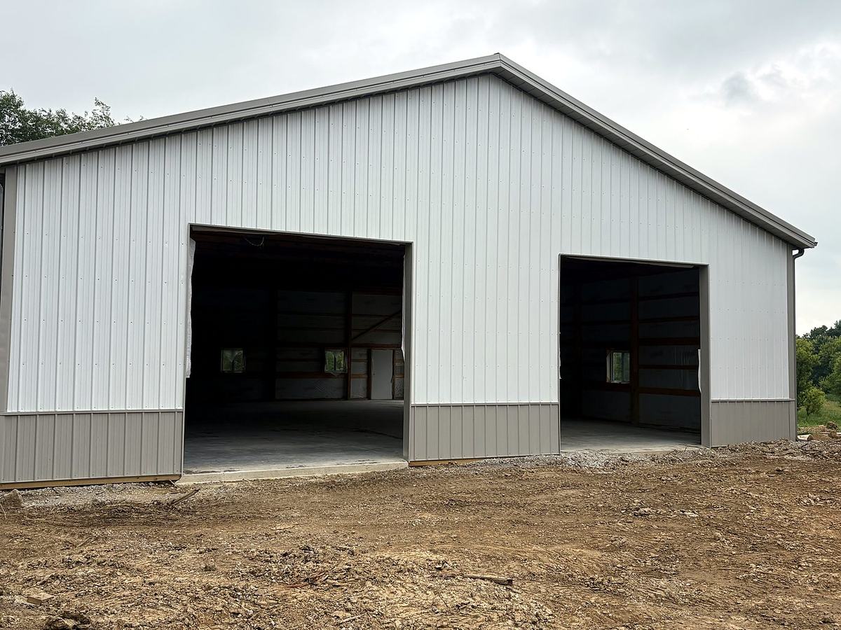 White pole barn with gray wainscot and two large door openings