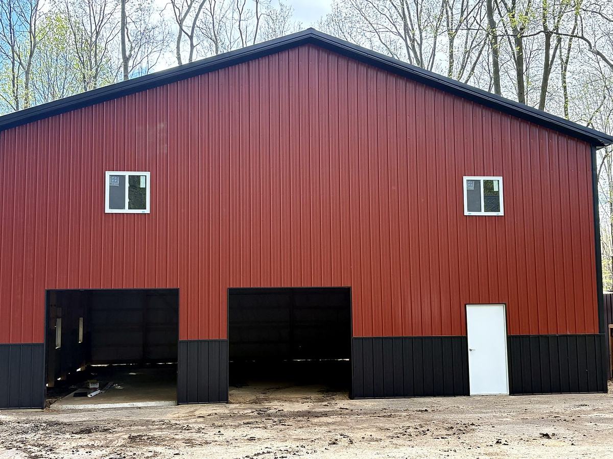 Red pole barn with black wainscot, three overhead doors and windows