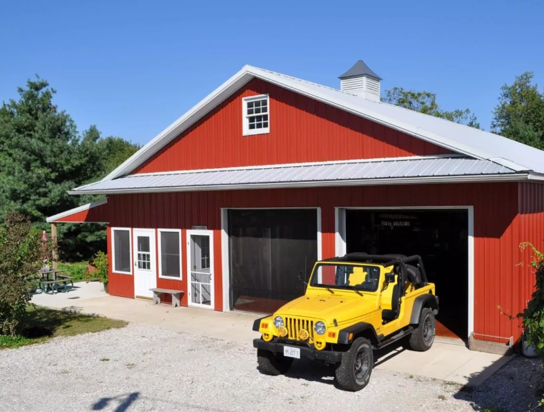 Custom red residential pole barn garage with white trim, overhead doors, and covered porch